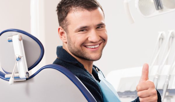 Smiling young man at dentist's surgery with thumb up